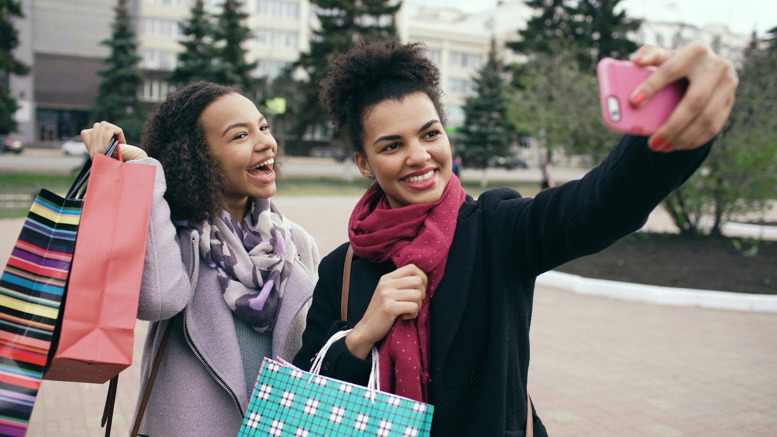 Two smiling friends with shopping bags taking a selfie on a phone